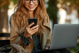 Woman smiling while looking at her cellphone and using a laptop